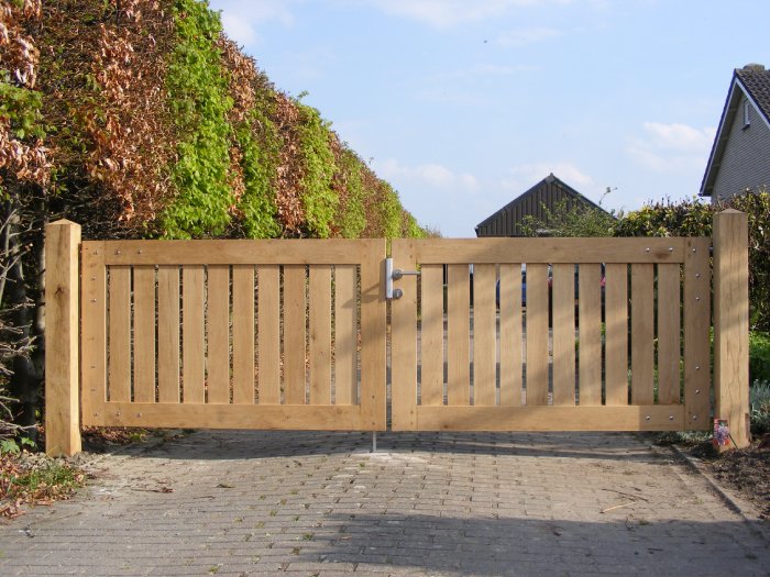 Houten toegangspoort bij oprit met dubbele draaideuren en strakke verticale belijning tussen groene hagen
